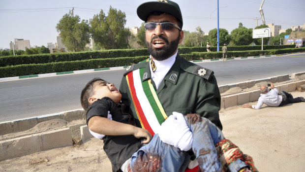 A Revolutionary Guard member carries a wounded boy after a shooting during a military parade marking the 38th anniversary of Iraq's 1980 invasion of Iran.
