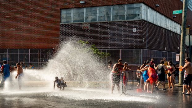 People stand in the spray of water coming from a fire hydrant in the Bronx borough of New York, US. 