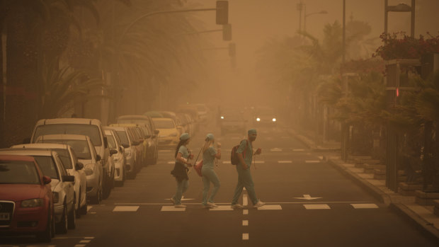 People in carnival dress walk across a street crossing in a cloud of red dust in Santa Cruz de Tenerife, Spain.