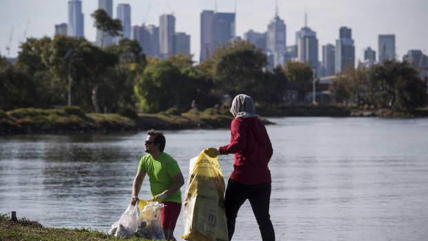 Derek Atkinson and  Farah Rozhan practise plogging along the Maribyrnong River trail at Footscray, with Melbourne CBD in the background. 