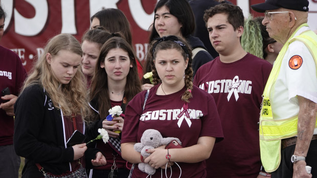 Students carrying flowers wait to cross the street after their first day back at Marjory Stoneman Douglas High School in Parkland, Florida.
