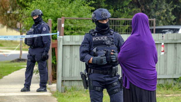 An armed police officer speaks to a woman as she arrives at the home of Shire Ali's parents in Werribee. 
