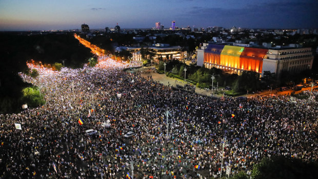 People shine the lights of their mobile phones during protests outside the government headquarters, seen at right.
