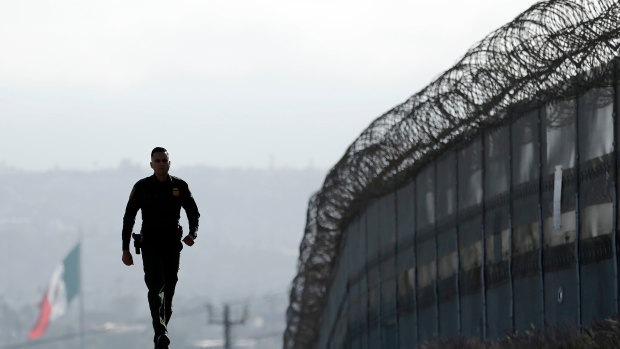 Border Patrol agent Eduardo Olmos walks near the secondary fence separating Tijuana, Mexico, background, and San Diego in San Diego, California.