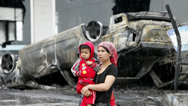 A Uighur woman and a child walk past a burnt car at a destroyed dealership  following riots in Urumqi, western China's Xinjiang province in 2009. Analysts say the riots set in motion the harsh security measures now in place.