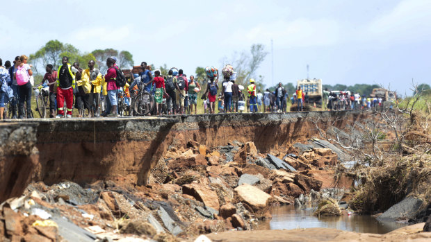 People pass through a section of the road damaged by Cyclone Idai in Nhamatanda in Mozambique.