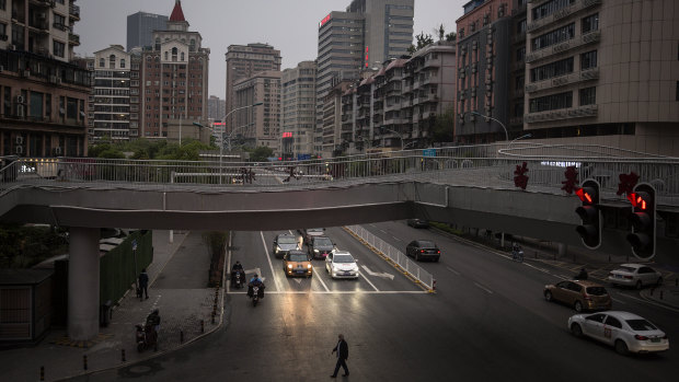 A resident crosses a road while cars wait for traffic lights on April 2 in Wuhan, Hubei, China, where residents with green health code are allowed to go out in public. 