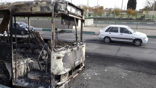 Cars in Tehran drive past a bus that was torched during protests that followed authorities' decision to raise petrol prices.