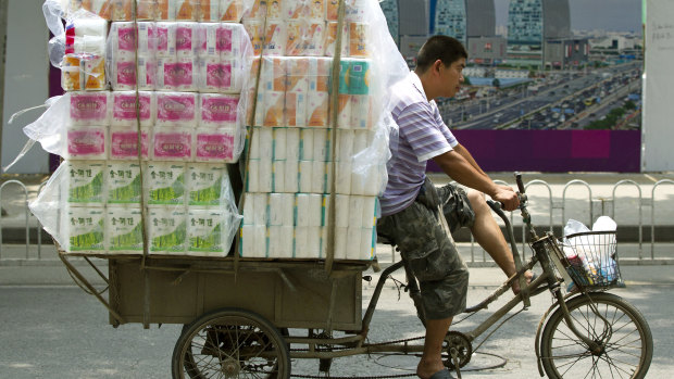 A tricycle porter transports packs of toilet paper in Beijing.