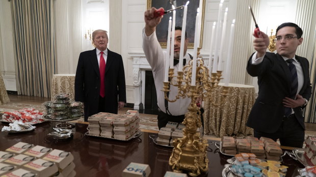US President Donald Trump presents the fast food to be served to the football players as White House workers light tapered candles.