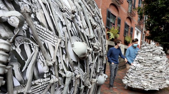 Protesters carry parts of a bone sculpture to set up outside the home of Moderna CEO Stephane Bancel to demand global vaccine equity.