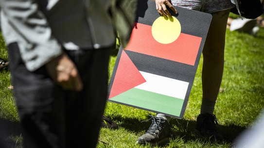 Flags and placards showing Indigenous solidarity with Palestine at a Melbourne rally.