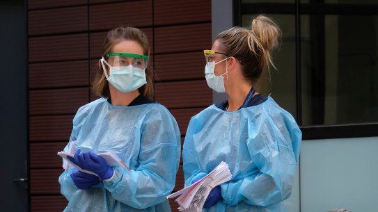 Hospital staff assist people waiting in line to be screened for COVID-19 outside the Royal Melbourne Hospital.