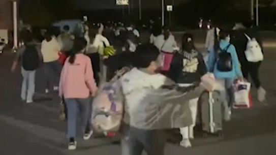 In this photo taken from video footage, people with suitcases and bags are seen leaving from a Foxconn compound in Zhengzhou.