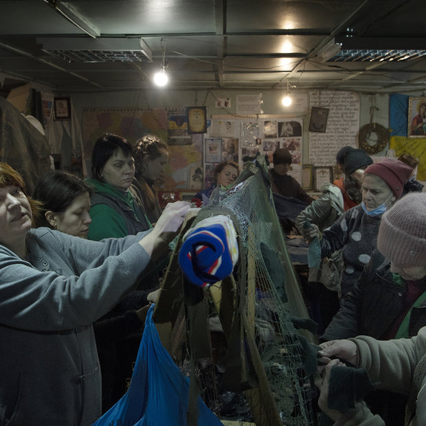 A group of women tie strips of donated material into camouflage nets in a shelter in Uman.