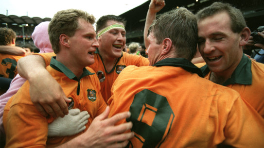 Michael Lynagh (left) is hugged by Phil Kearns (taped head) as they embrace Australian captain Nick Farr-Jones as they celebrate victory at the final whistle. Winger Bob Egerton is on the right.