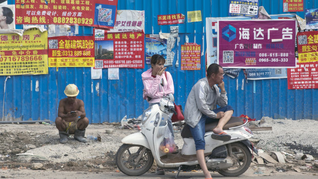 People wait in front of advertisements in Chinese pasted on a fence outside a construction site in Sihanoukville, Cambodia.