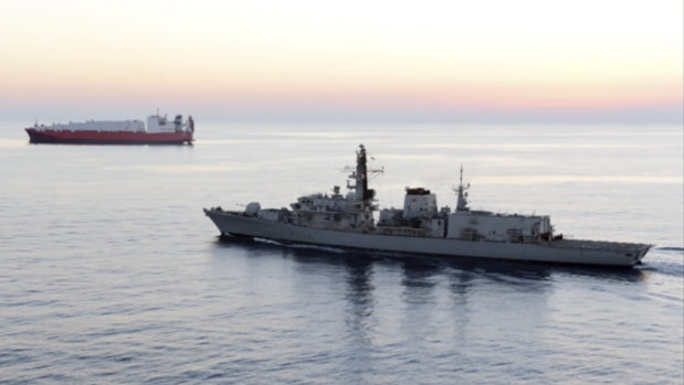 HMS Montrose accompanies a commercial ship through the narrow Strait of Hormuz.