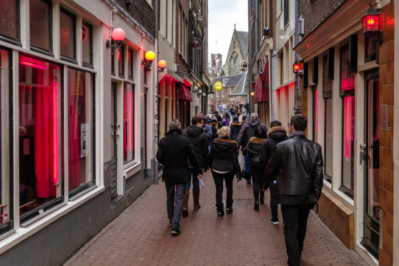 Tourists walk in the “red light district” of Amsterdam, where prostitutes try to lure customers from behind their window.