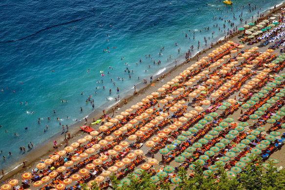 An aerial photograph of tourists playing and sunbathing on a sandy beach in Positano, Italy.