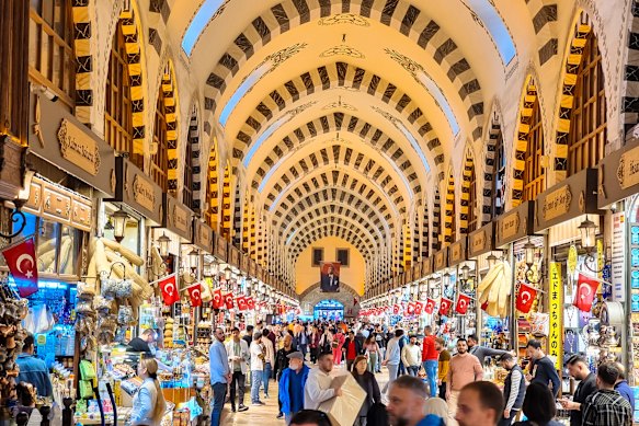 Crowds of visitors walk beneath vaulted stone arches at the Grand Bazaar in Istanbul, Turkey.