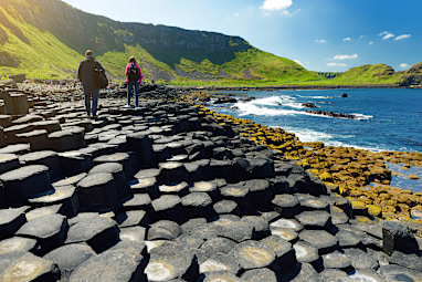 Two tourists walking at Giants Causeway, an area of hexagonal basalt stones