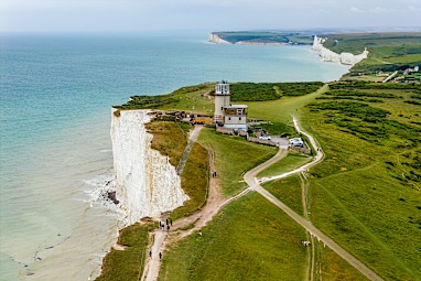 Eroding clifftop path near Belle Tout lighthouse with tourists walking on coastal path - Seven Sisters Cliffs Walk
