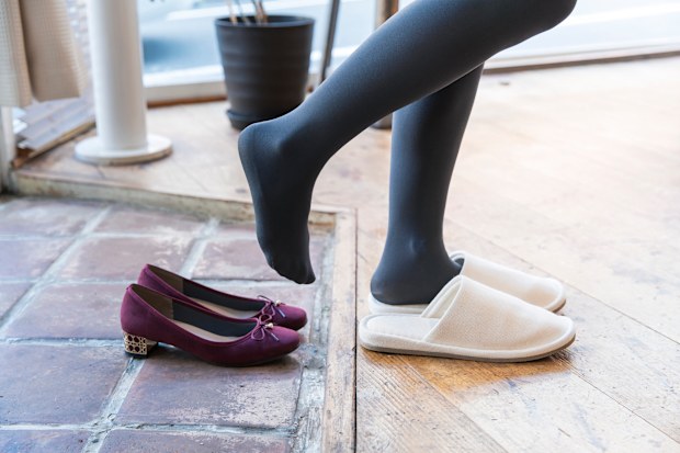 A woman comes home and takes off her shoes and wears indoor slippers