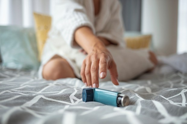 Girl suffering asthma attack reaching inhaler sitting on a bed in the bedroom at home. Woman Hand Reaching Inhaler Because She Suffering From Asthma Attack