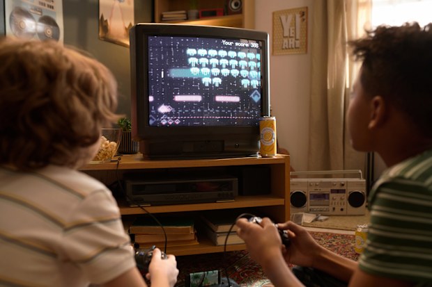 Back view of two kids absorbed in playing a retro video game on CRT TV