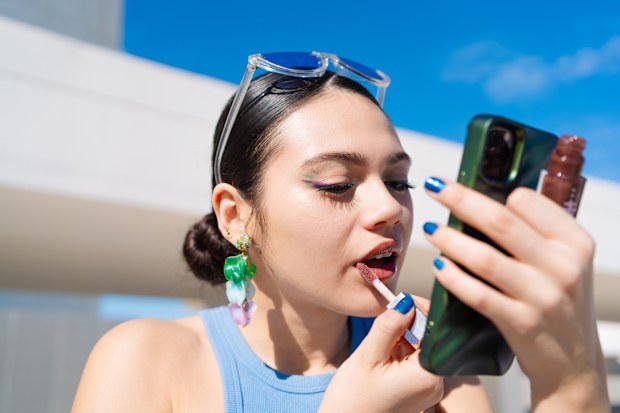 Stock image of a young woman applying lip gloss
