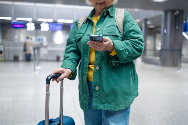 senior 60s woman in comfy casual outfit in airport, holding a smartphone 
