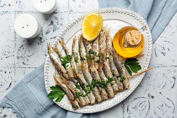 f Grilled Sardines skewers on a white plate with lemon and olive oil. Mediterranean food.