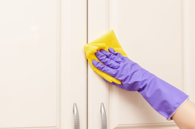 Kitchen cupboard door being wiped clean with a cloth.