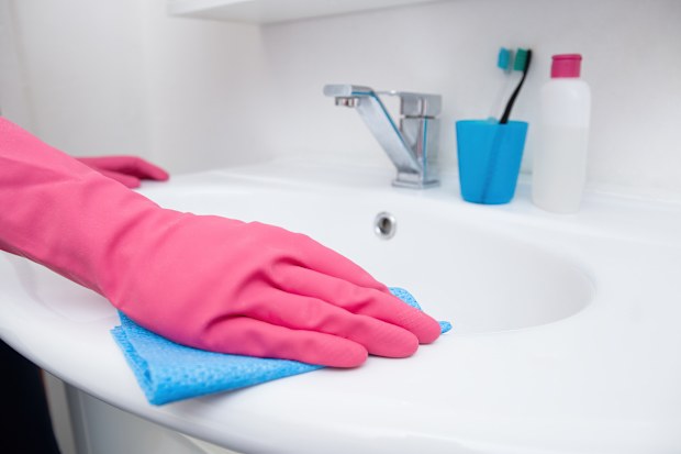 Person cleaning bathroom basin while wearing pink gloves