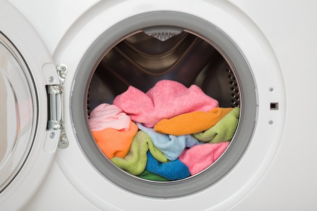 White opened washing machine full of colorful microfiber cleaning rags.