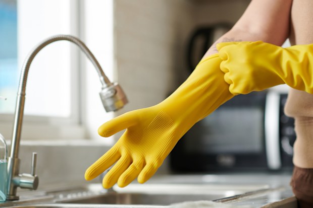 woman putting on rubber yellow protective gloves to wash dishes in kitchen