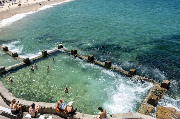 Sydney, Australia - Nov 29, 2022: Swimmers and sunbathers enjoying the warm summer weather at the Ross Jones Rockpool at Coogee Beach. White water crashing into the rockpool.