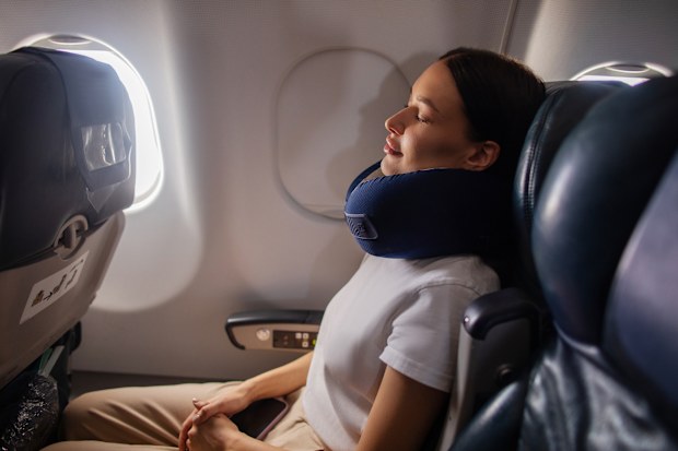 Peaceful cabin nap. Lady sitting in plane seat near closed window with neck pillow, her eyes closed, enjoying time during the flight, side view