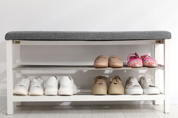 Shoe storage bench with different footwear near white wall indoors