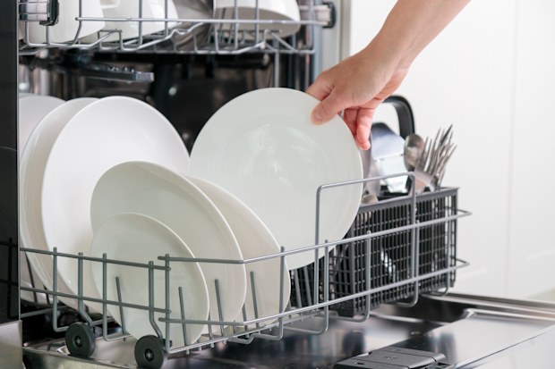 Female hand unloading dishwasher with tableware.