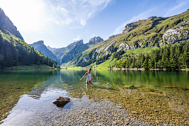Young woman wading in clear mountain lake surrounded by the swiss alps