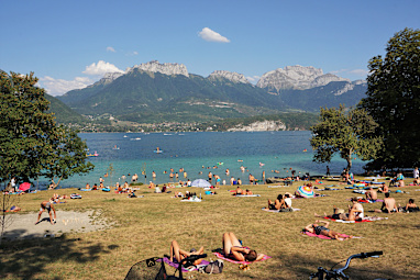 Holidaymaker are sunbathing on a grassy bank beside lake Annecy, France A traffic-free cycle path runs beside this sunbathing area.