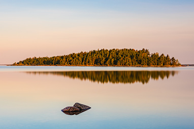 Calm waters of Lake Vanern Sweden reflect the soft morning light, showcasing an island enveloped by lush greenery.