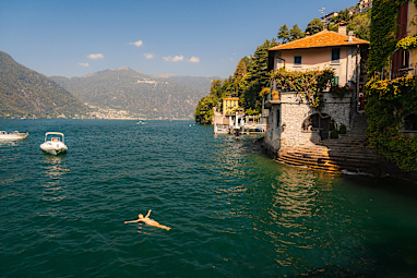 Woman swimming in Como lake near quaint Italian town during vacation in summer