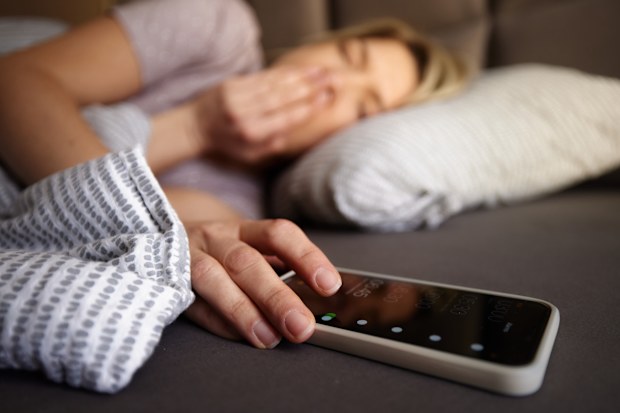 Woman turning off her alarm clock on smart phone while waking up in a bed.