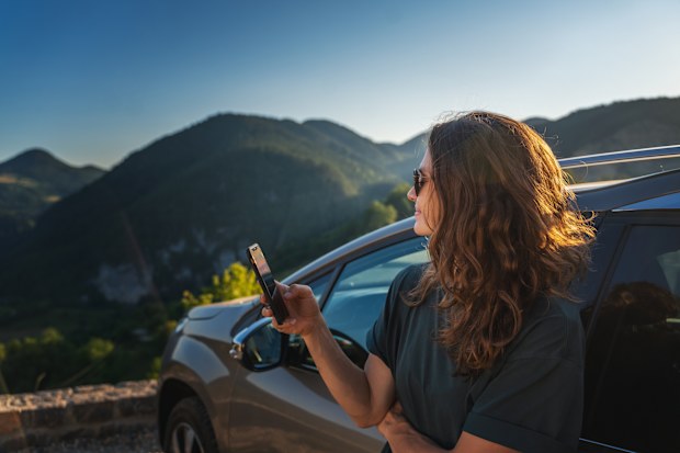 Young beautiful woman traveling by car in the mountains using smartphone at sunset