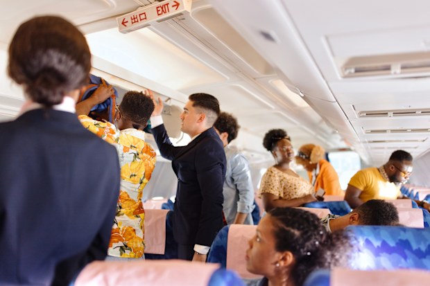 Cabin Crew helps passenger with putting bags and suitcases in overhead locker