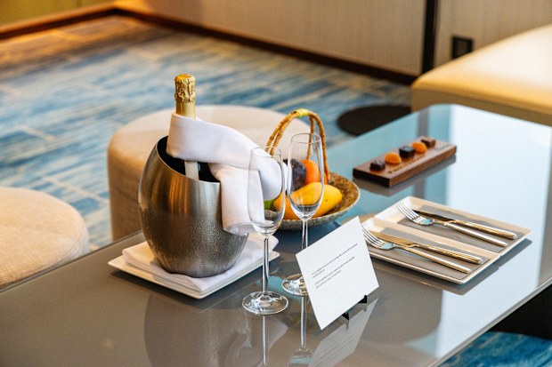 Luxury hotel room with champagne, fruit basket, and chocolate on glass table.