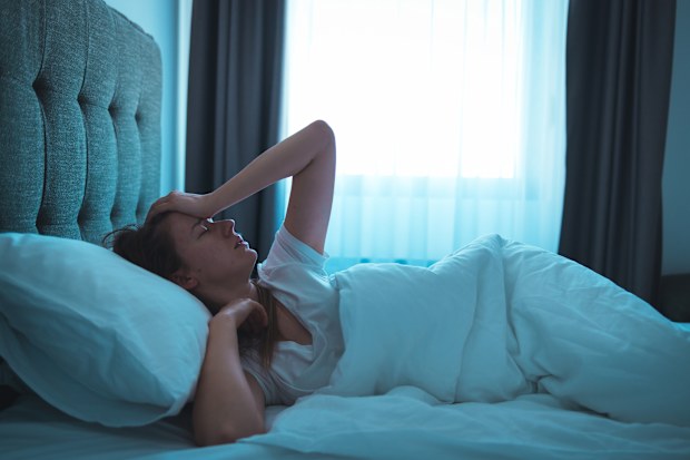 Photo of a young woman lying in bed at night, wide awake with a case of insomnia